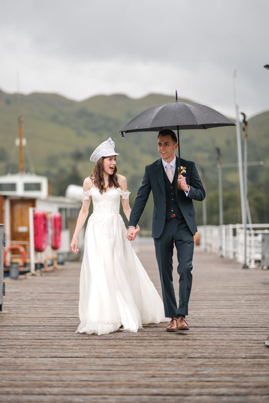 Wedding couple walking on the pier with umbrella in the rain at Inn on the Lake