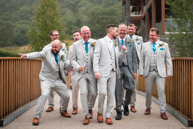Lodore Falls Hotel groomsmen relaxed wedding portrait Groomsmen walking across a bridge laughing at Lodore Falls Hotel wedding in the Lake District