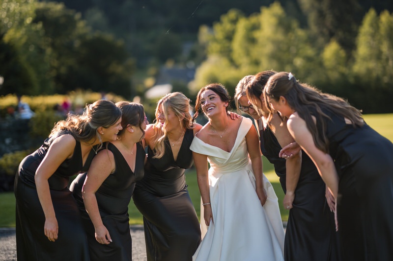 Bride and bridesmaids laughing together in a group hug during a summer wedding at Inn on the Lake