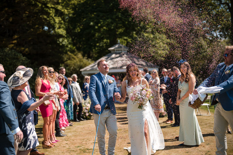 Bride and groom walking through colourful confetti tunnel at Lake District wedding