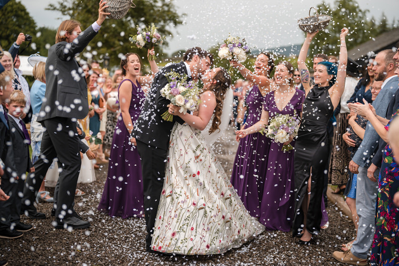 Friends throwing dried petal confetti over couple outside a modern Lake District wedding venue