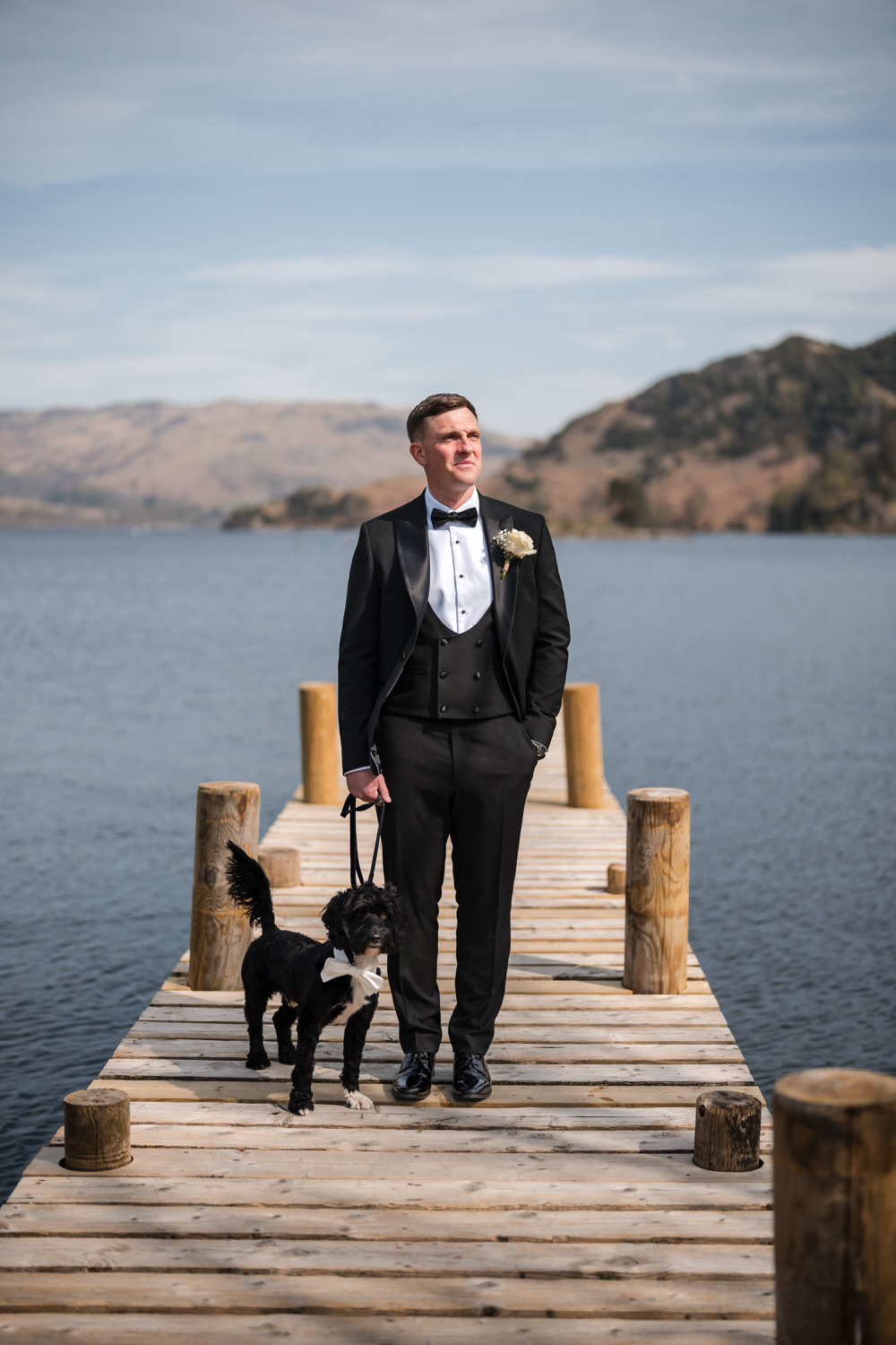 Groom standing on an Ullswater jetty with his dog at a Lake District wedding