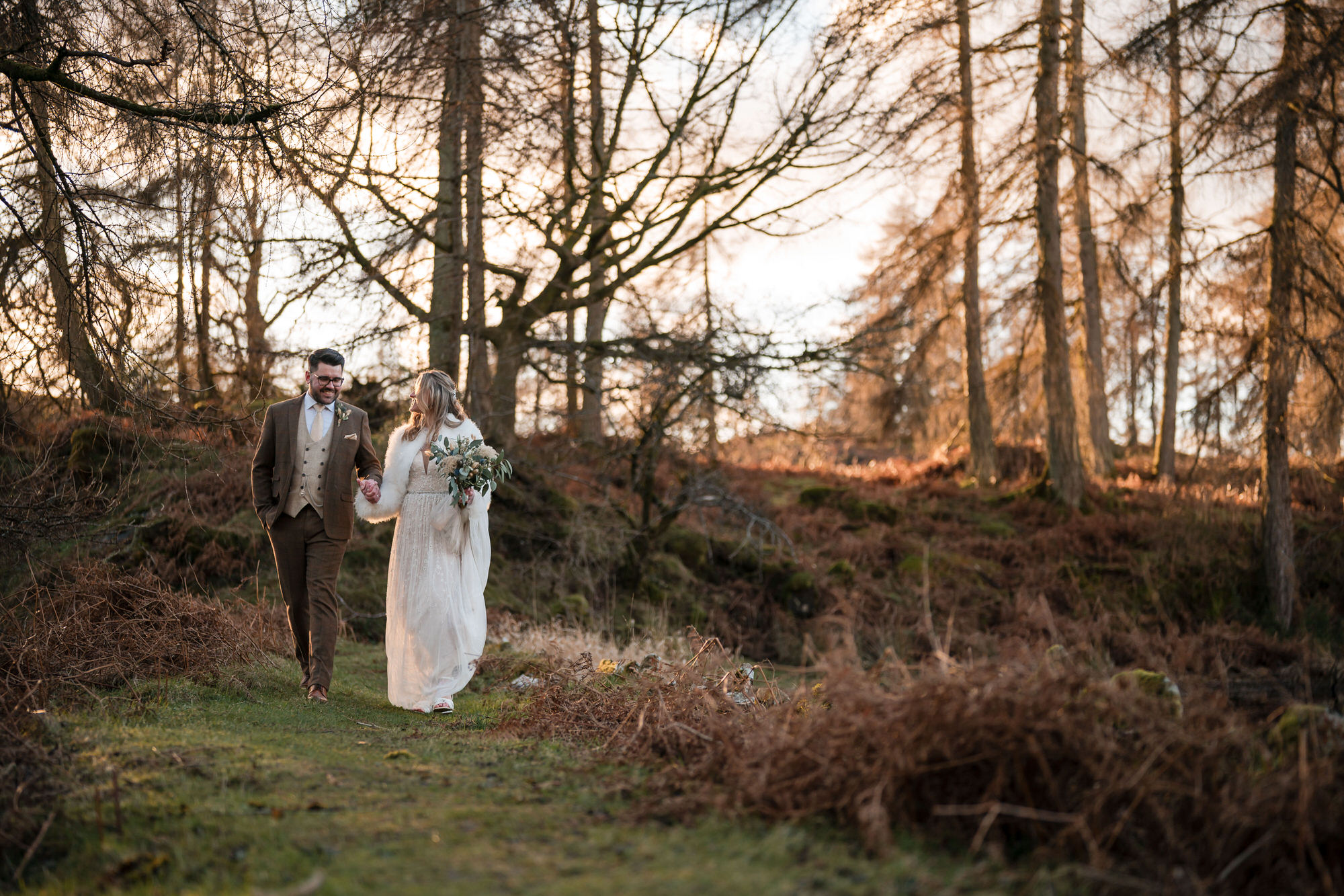 Winter wedding couple walking through woodland at Gilpin Lake House
