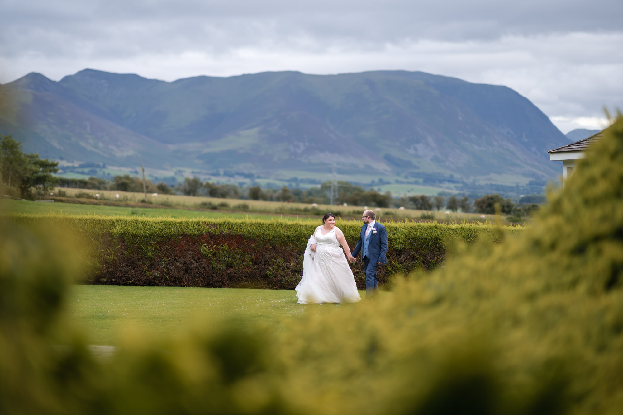 Wedding couple walking on the garden lawn at Hundith Hill Hotel with fells behind them