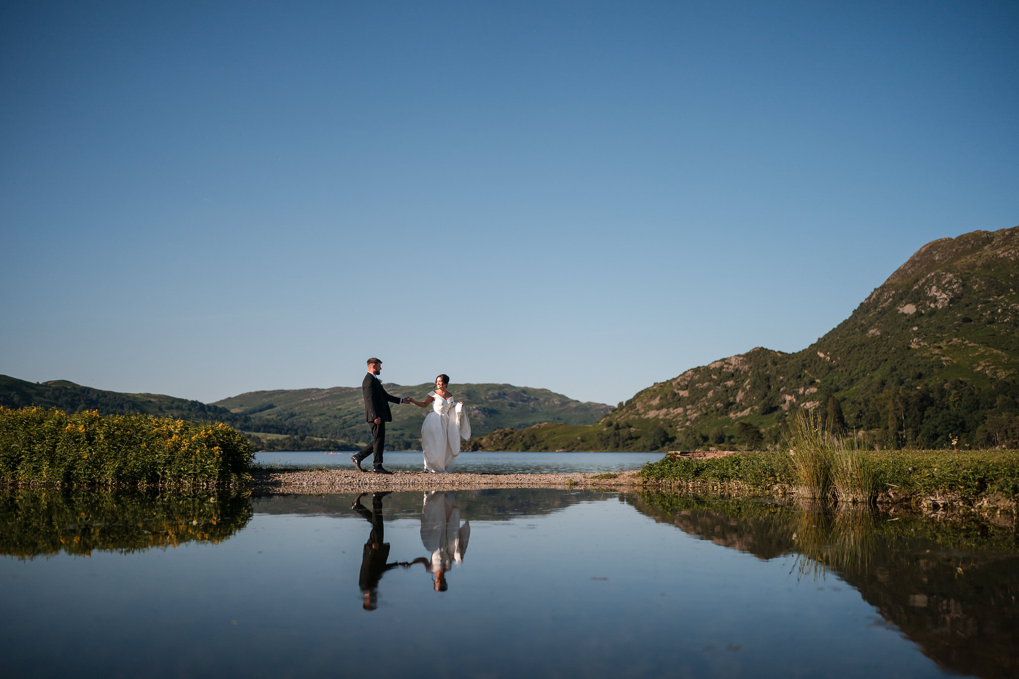 Dan and Amy walking beside Ullswater reflected in the calm garden pool