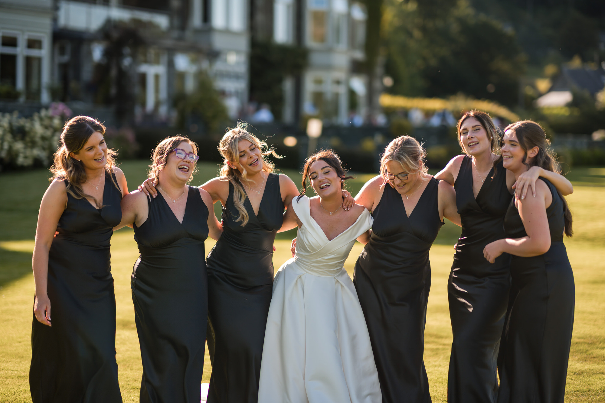 Amy laughing with her bridesmaids in golden evening light on the lawn