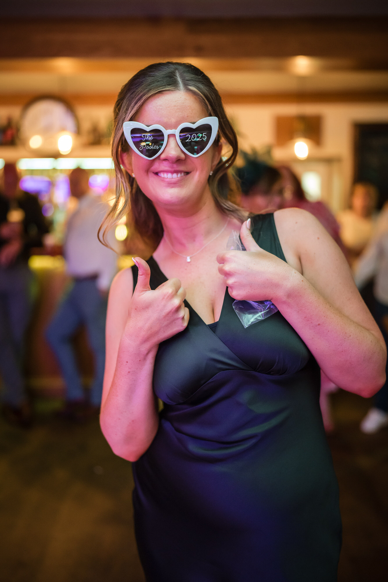 A bridesmaid giving two thumbs up in personalised heart-shaped glasses