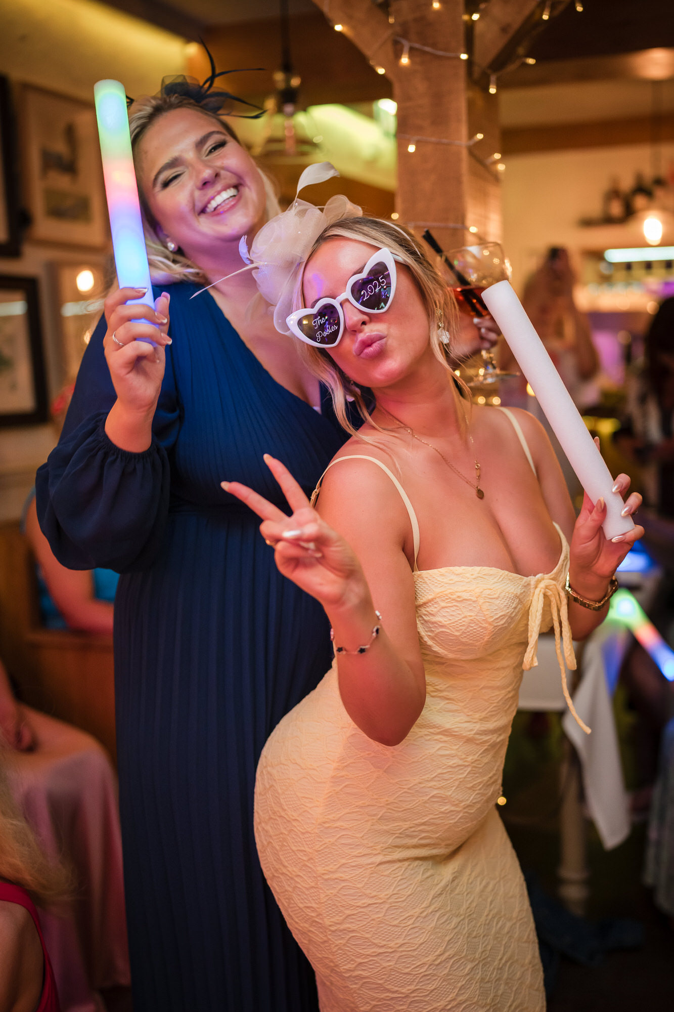 Two guests posing with glow sticks and wedding party glasses