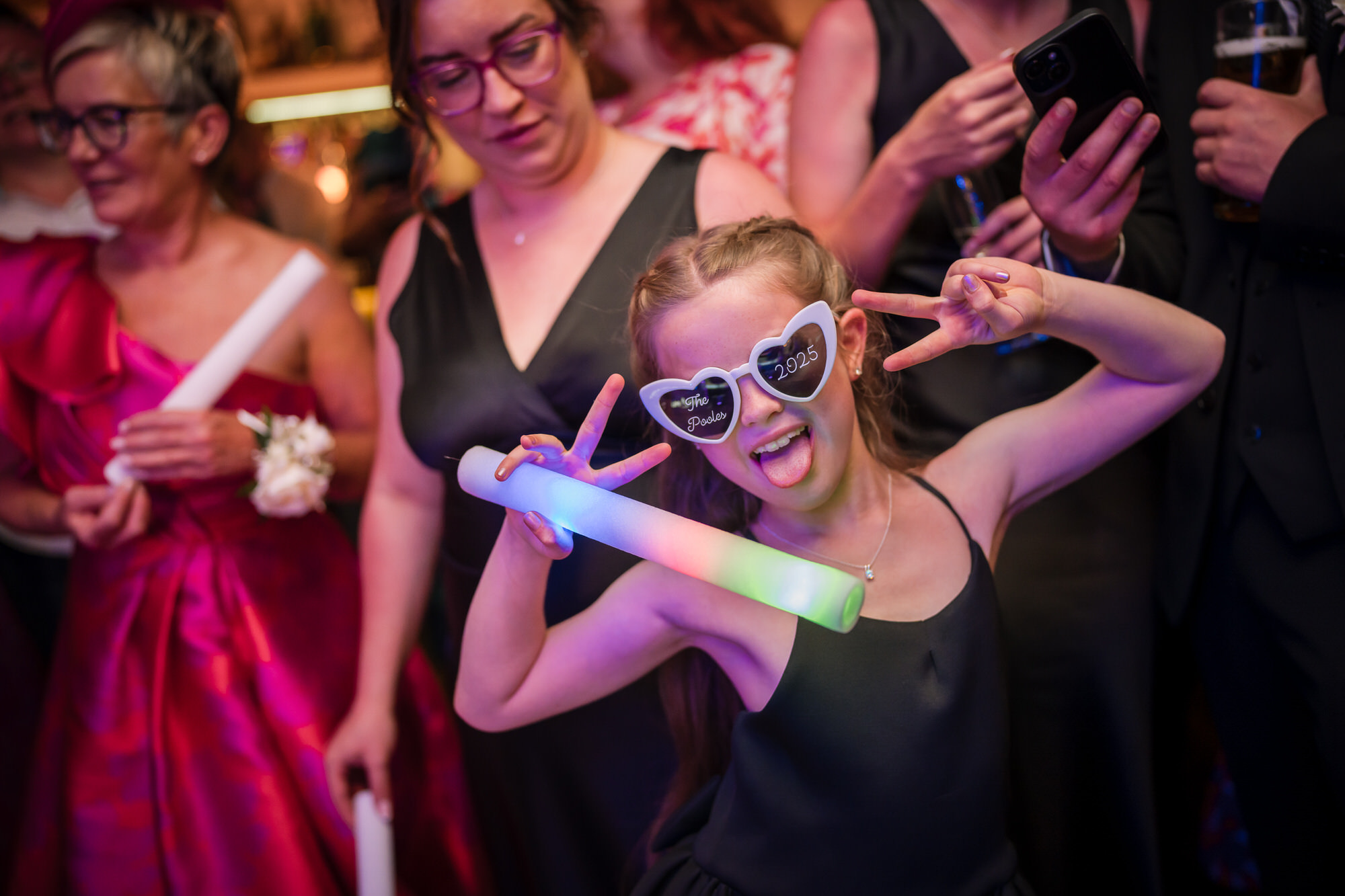 A young guest posing with heart-shaped glasses and a glowing foam stick