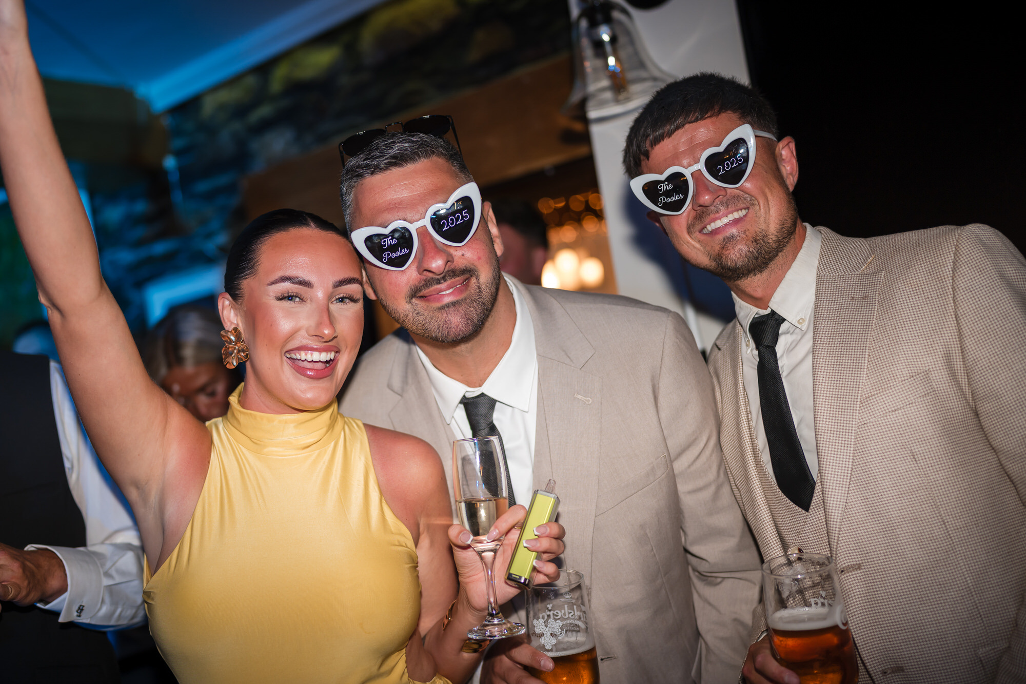 Wedding guests celebrating in The Pooles 2025 heart-shaped party glasses