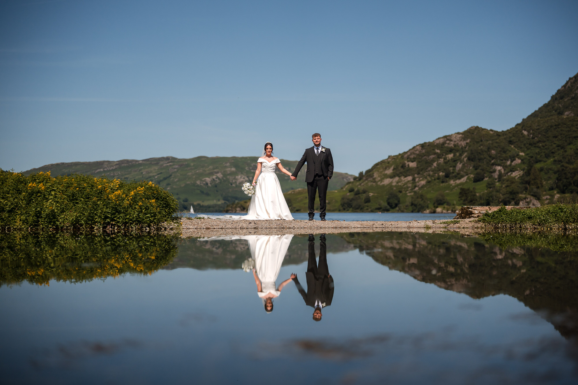 Dan and Amy holding hands beside Ullswater with a mirror reflection in the garden pool