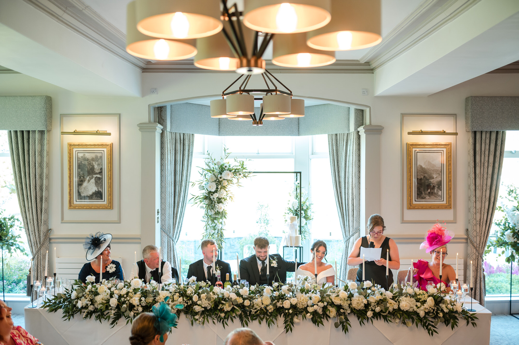 Top table decorated with abundant white flowers during the wedding speeches