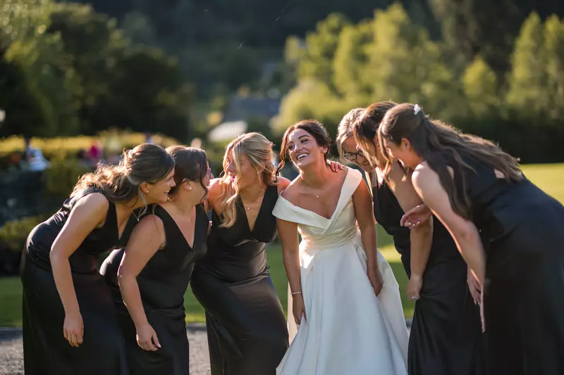 Inn on the Lake bride and bridesmaids laughing group hug summer wedding Bride and bridesmaids laughing together in a group hug during a summer wedding at Inn on the Lake