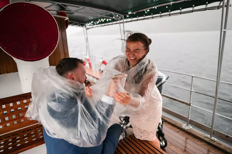 Wedding guests laughing in rain ponchos aboard a boat on Ullswater