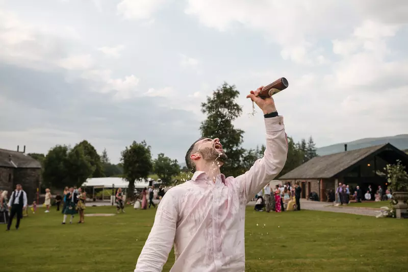 Wedding guest celebrating with a beer shower at New House Farm in the Lake District