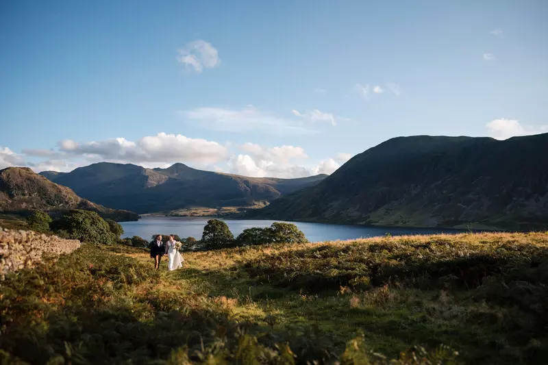 New House Farm Lorton wedding wide Lake District landscape portrait Wedding couple walking through a wide Lake District valley landscape near Lorton with a lake in the distance