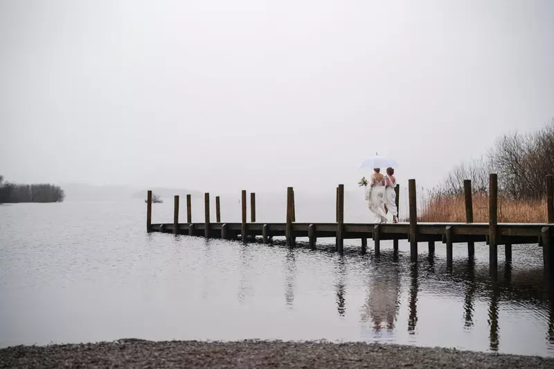 Lesbian wedding dock walk with an umbrella at Lodore Falls Hotel