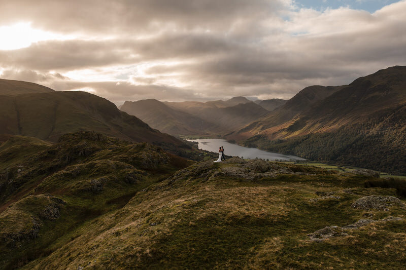 Lake District mountain elopement ridge epic landscape portrait Epic wide Lake District landscape with a wedding couple standing on a high ridge above a valley and lake