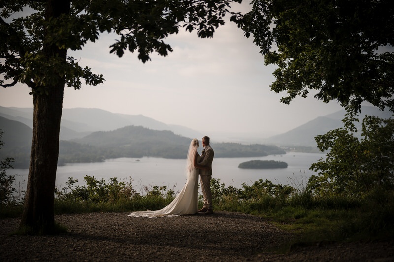 Silhouette wedding couple standing beneath trees overlooking a Lake District lake and distant hills