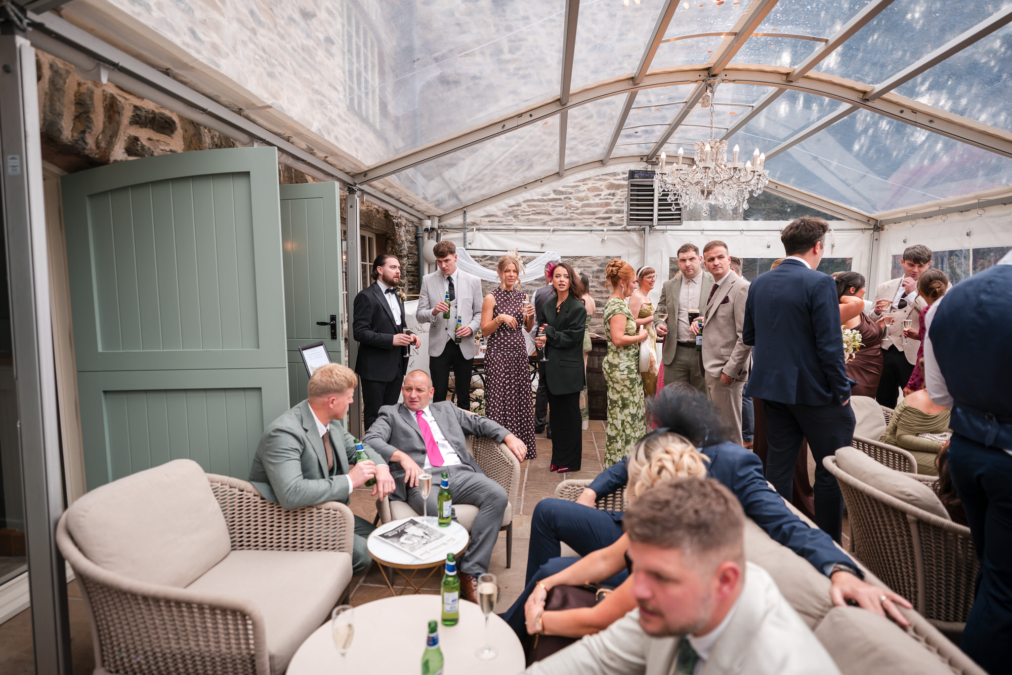 Wedding guests relaxing in the bright conservatory during the drinks reception
