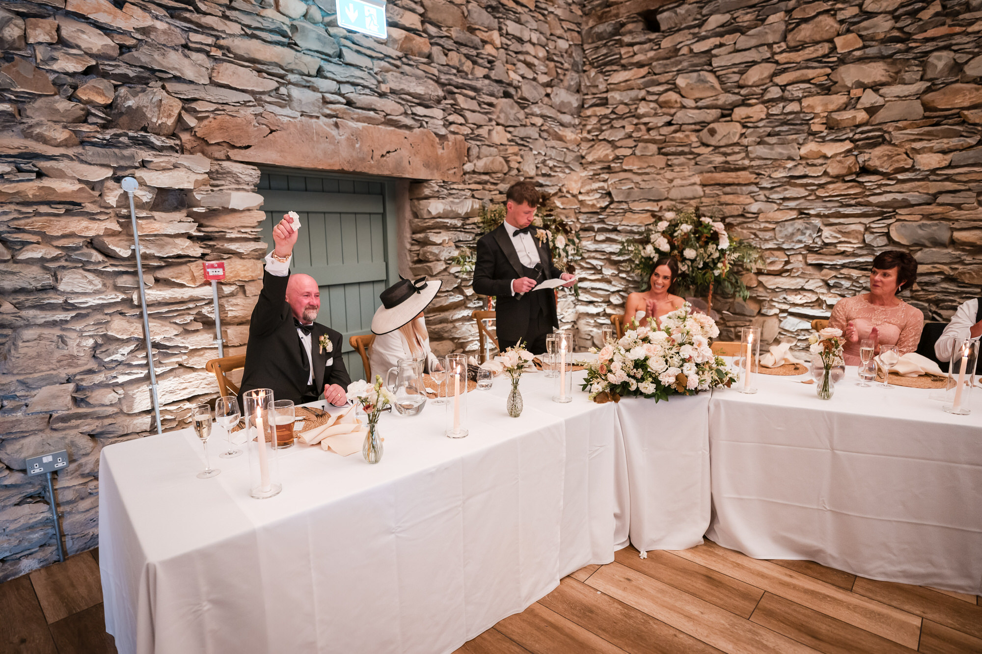 A wedding speech at the flower-decorated top table in the stone barn